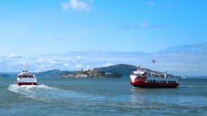 Red and White Fleet cruise boats sailing past Alcatraz Island in the San Francisco Bay.