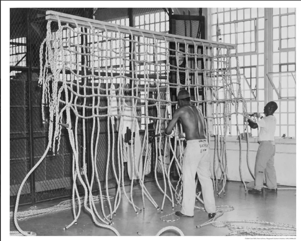 Black and white historical photo of Alcatraz inmates in a large workshop weaving heavy-duty rope cargo nets for the U.S. Navy during the World War II era
