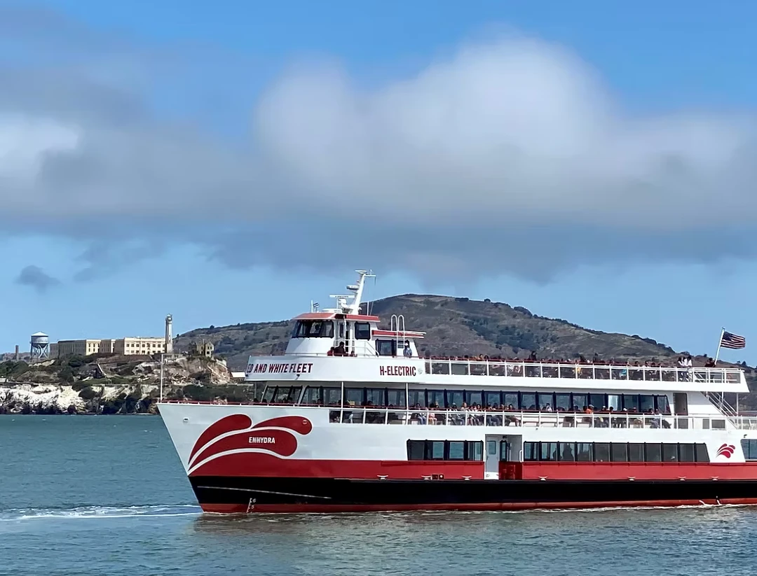 Red and White Fleet's Enhydra hybrid-electric tour boat cruising in San Francisco Bay with Alcatraz Island in the background.