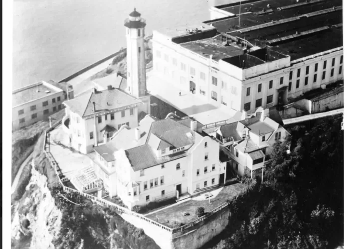 A historical aerial photograph showing the 15-room Warden's House mansion and the adjacent 84-foot reinforced concrete Alcatraz Lighthouse on the island’s summit during the 1940s.
