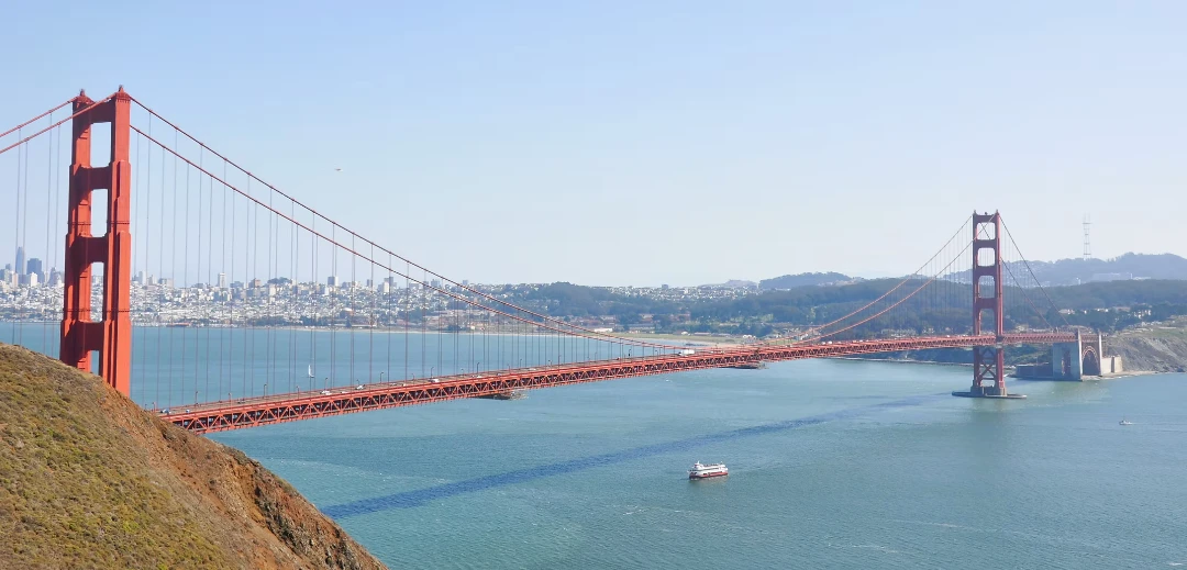 A Red and White Fleet bay cruise boat sailing on the San Francisco Bay with a wide-angle view of the Golden Gate Bridge and City skyline of San Franciosco.