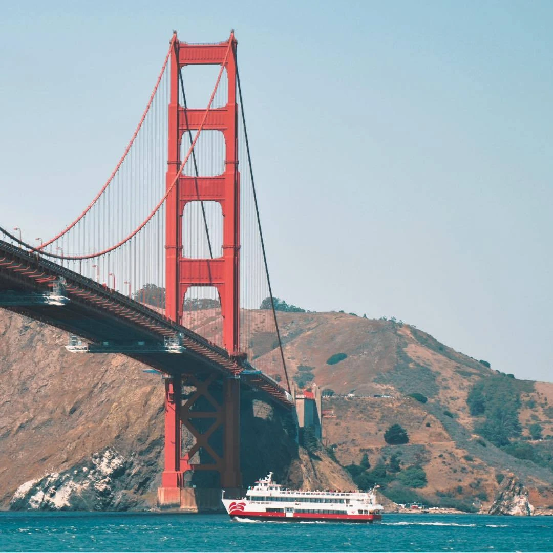 A close-up view of a Red and White Fleet boat sailing directly under the massive north tower of the Golden Gate Bridge.