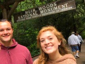 Two guests standing at the entrance sign of Muir Woods National Park during a guided tour from San Francisco