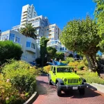 Tour guests standing in an open-air Jeep while traveling downhill on Lombard Street during a private San Francisco sightseeing tour