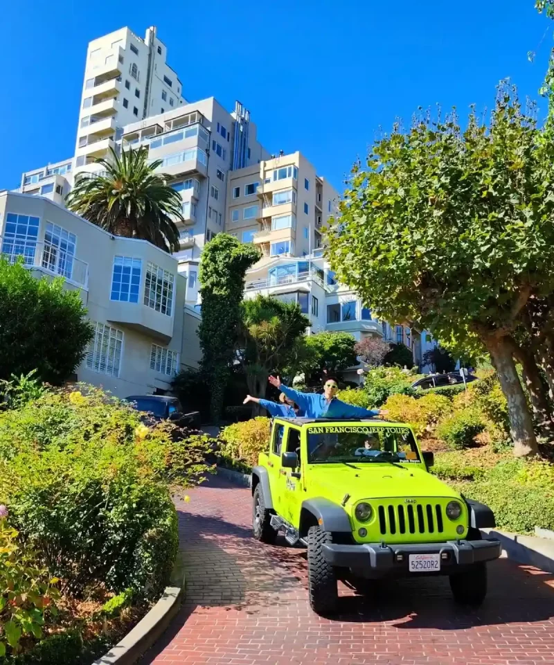 Tour guests standing in an open-air Jeep while traveling downhill on Lombard Street during a private San Francisco sightseeing tour