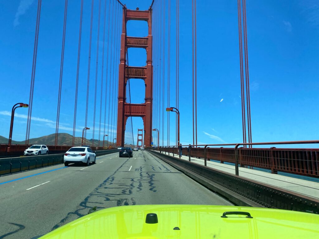 View from inside an open-air Jeep traveling over the Golden Gate Bridge with the tower ahead