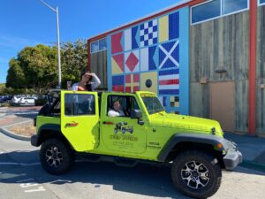 Guests standing with an open-air Jeep in Sausalito in front of a nautical flag tile mural