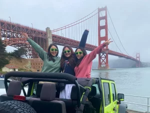 Three guests standing in an open-air Jeep during a private San Francisco sightseeing tour with the Golden Gate Bridge in the background