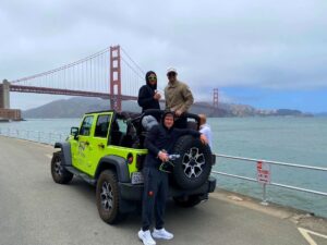 Open-air Jeep with guests in the foreground as fog hangs over the Golden Gate Bridge and San Francisco Bay