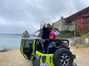 Tour guests in an open-air Jeep at Fort Baker with fog partially covering the Golden Gate Bridge during a San Francisco sightseeing tour