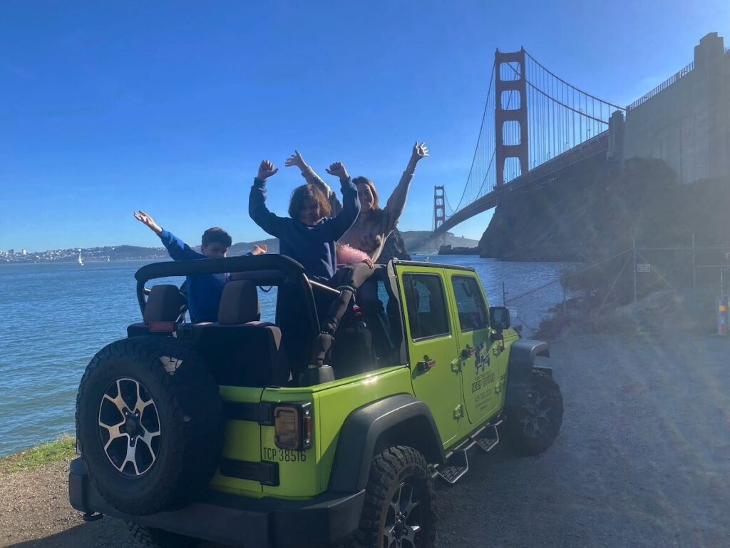 Tour guests in an open-air Jeep at Fort Baker beneath the Golden Gate Bridge North Tower during a San Francisco sightseeing tour