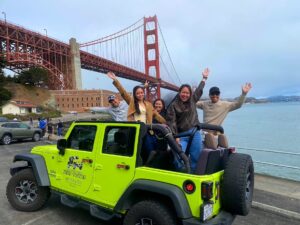 Tour guests riding in an open-air Jeep at Fort Point with the Golden Gate Bridge in the background during a San Francisco sightseeing tour